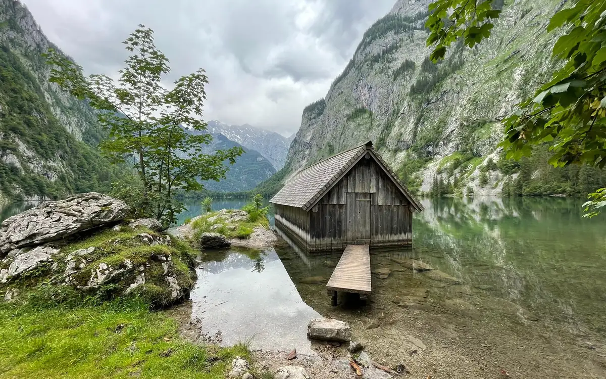 A weathered wooden boathouse with a small jetty on a clear lake between steep rock walls
