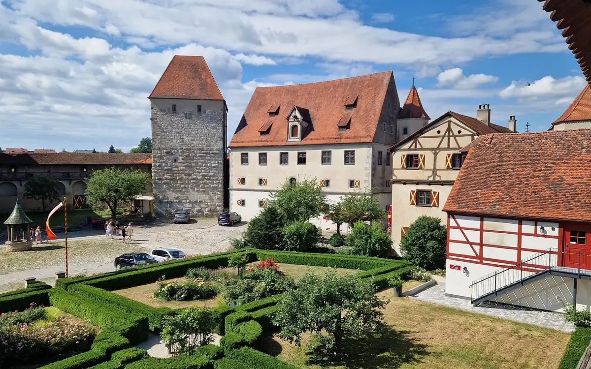 Ein Schlosshof mit Heckengarten, roten Dächern und einem Steinturm