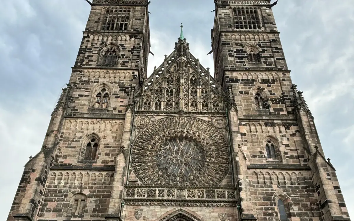 Eine gotische Kirchenfassade mit zwei quadratischen Sandsteintürmen und einer großen Fensterrose