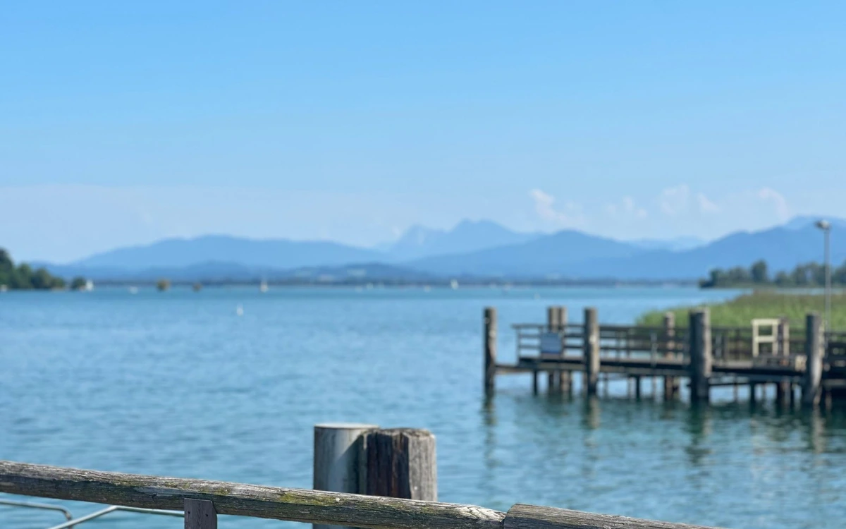 A weathered wooden jetty on Chiemsee, blue water and a line of hazy mountains along the far shore