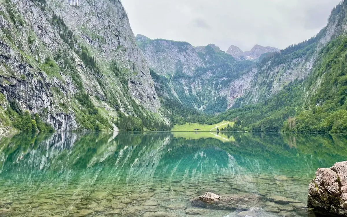 Steep rock walls and a green valley reflected in a clear green lake