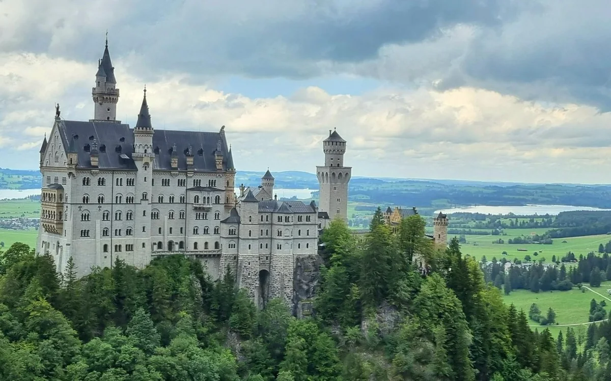 Neuschwanstein Castle über Wald, dahinter Seen und Felder