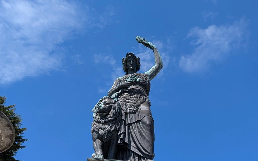 Die bronzene Bavaria-Statue mit ihrem Löwen vor blauem Himmel