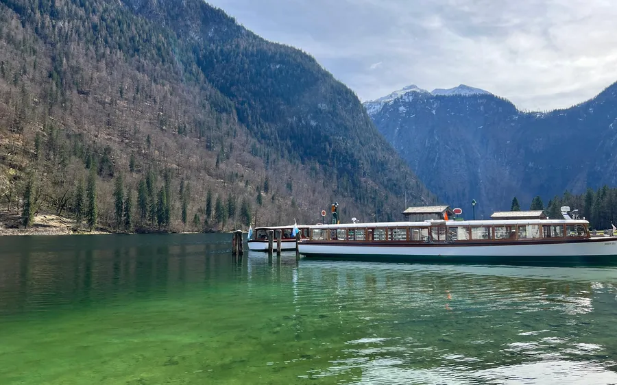 Ein Ausflugsboot am Steg auf grünem Wasser unter bewaldeten Bergen