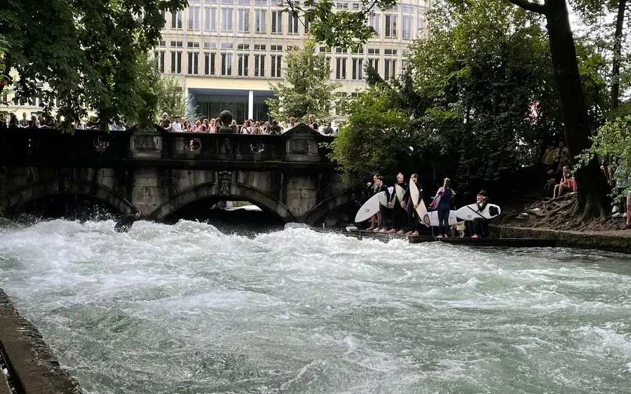 Surfer mit Boards neben einer schnellen stehenden Welle an einem Stadtfluss