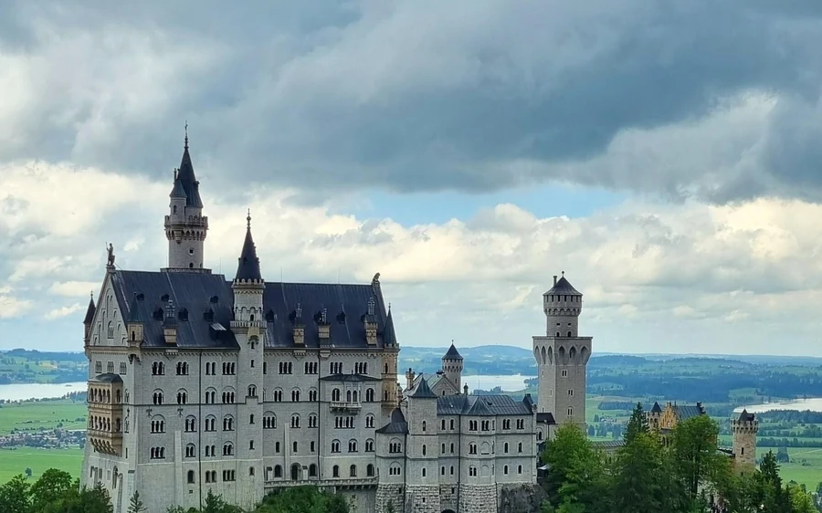 Neuschwanstein Castle unter schweren Wolken, dahinter Seen in der Ebene