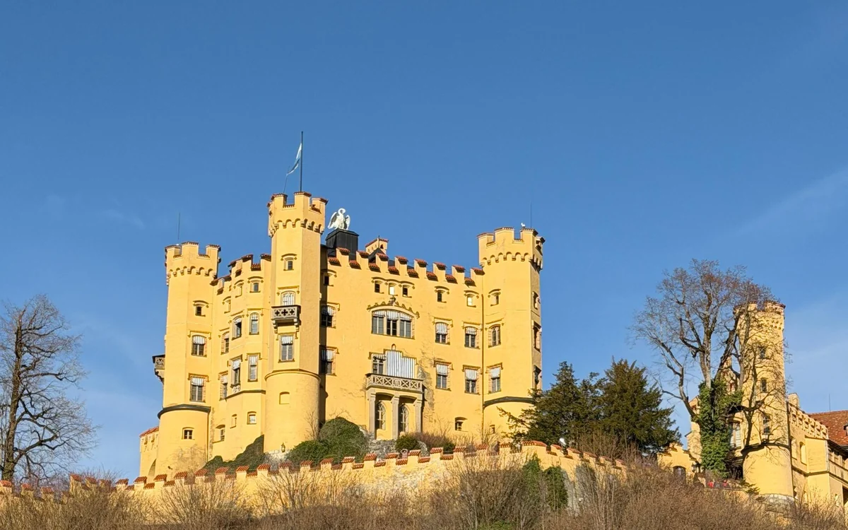Die gelben Mauern und Türme von Schloss Hohenschwangau auf seinem Hügel